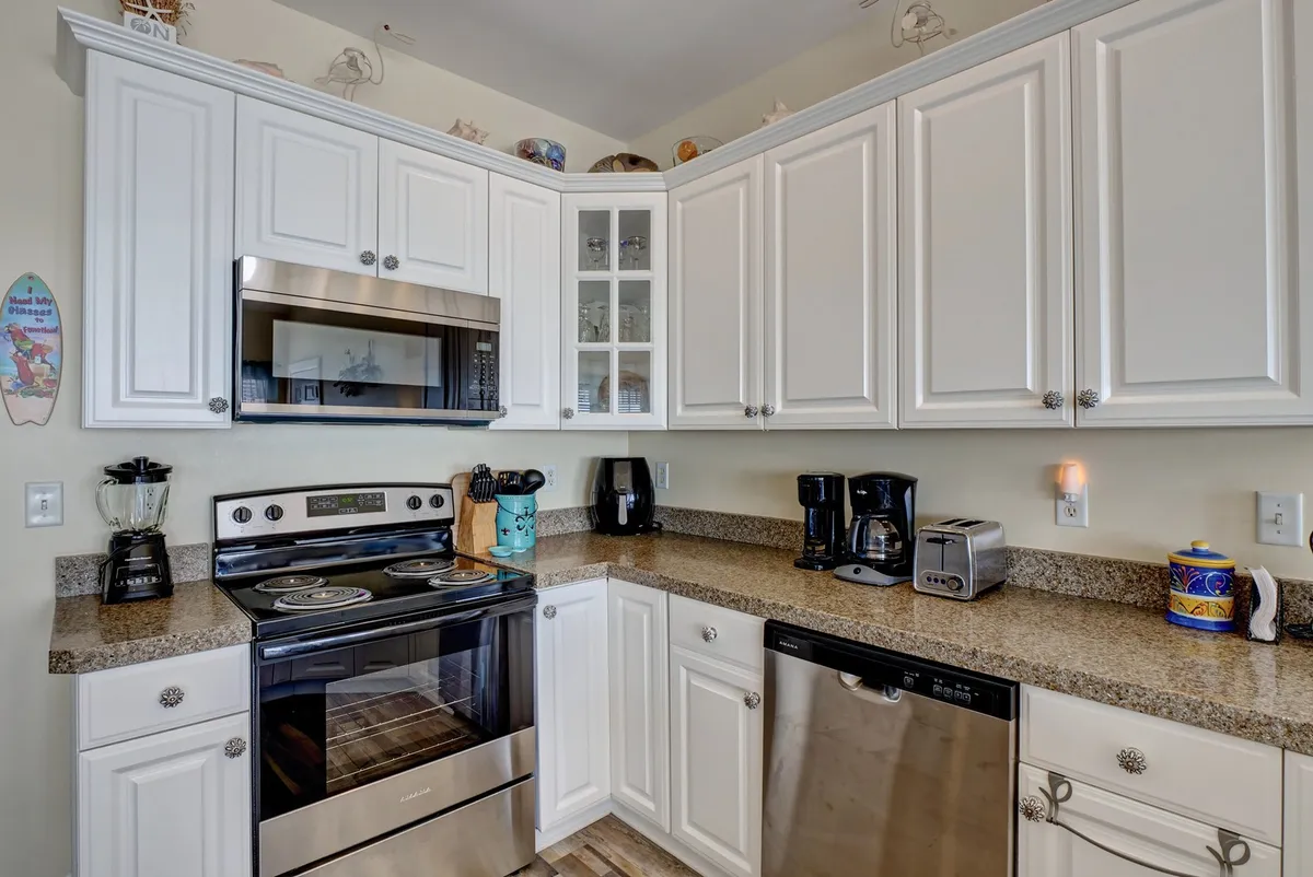 A modern, well-equipped kitchen with stainless steel appliances, a granite countertop, sleek white cabinetry, and decorative accents. The layout includes bar stools at the granite breakfast bar, inviting both casual meals and conversations. Warm lighting and thoughtful details make the kitchen feel both functional and welcoming.