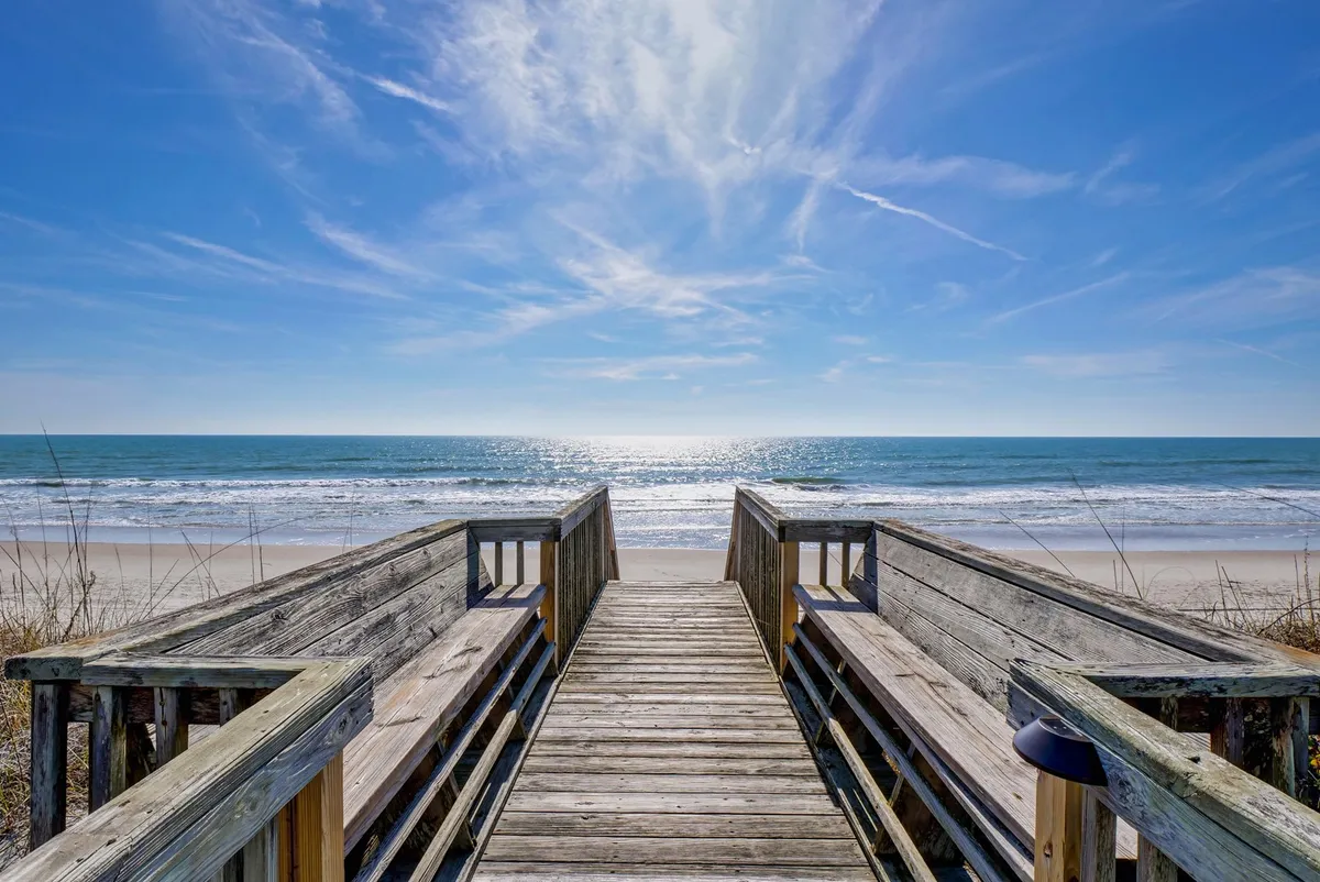 An exterior shot of a wooden walkway with an ocean view and wide open sky, leading guests from the home toward the beach. The clean, accessible path embodies both ease of access and natural beauty.