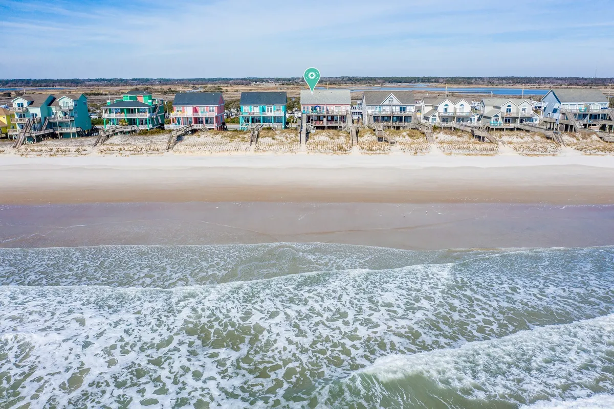 A cheerful, sunny scene featuring colorful beach houses lined up along a sandy beach and gentle waves lapping at the shore. The image captures a playful, welcoming atmosphere perfect for family gatherings, fishing, or quiet relaxation.