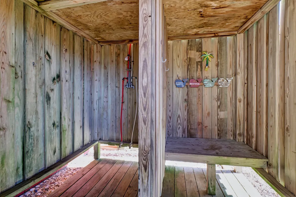 An interior view of the enclosed outdoor shower, showing wooden walls, a shower fixture, and a built-in bench. The space is functional and inviting, ideal for rinsing off after time at the beach.