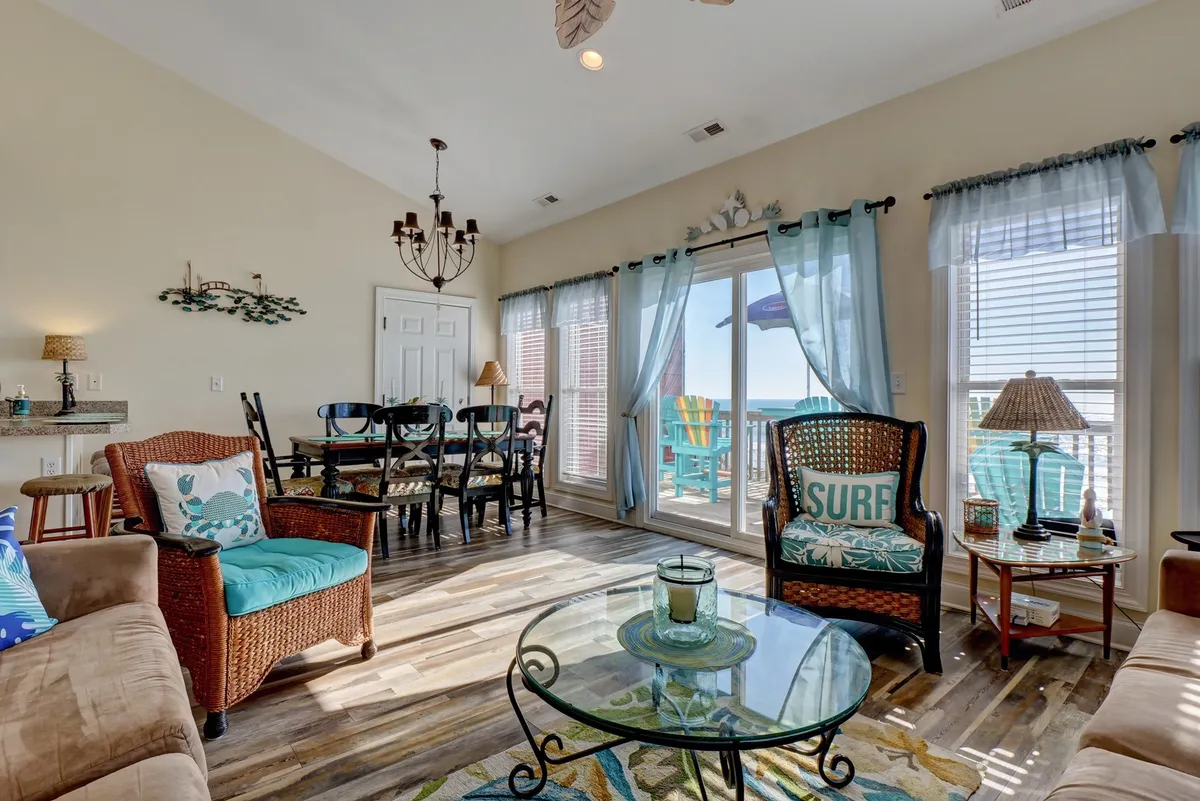 A bright, inviting interior with large windows framing an ocean view, a comfortable dining table, and relaxed seating. The scene is perfect for gathering with friends or family after a day of adventure, playing games, or streaming a show together.