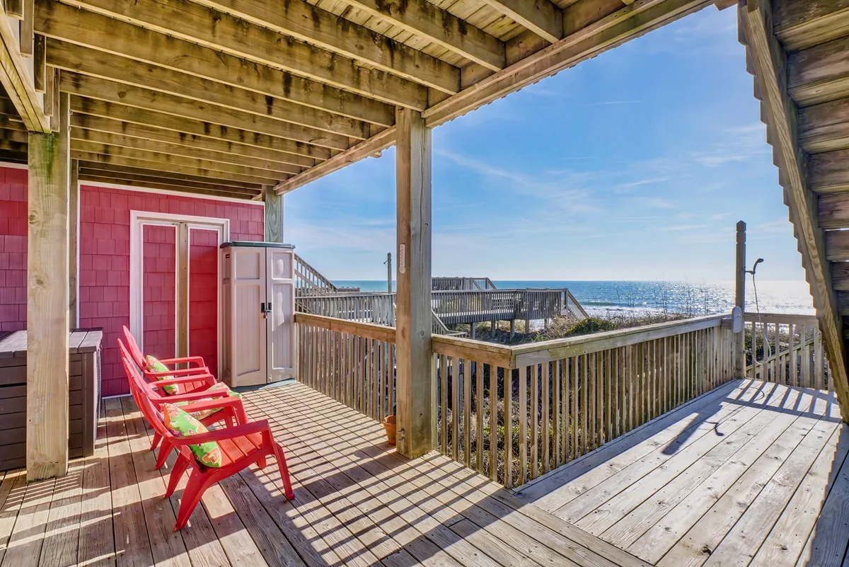 A tranquil wooden deck furnished with red chairs, all oriented toward a sweeping ocean view. The space feels peaceful, ideal for quiet moments, conversation, or soaking in the sound of the surf. The image captures the sense of transformation at different times of day, from sunrise serenity to lively evening gatherings.